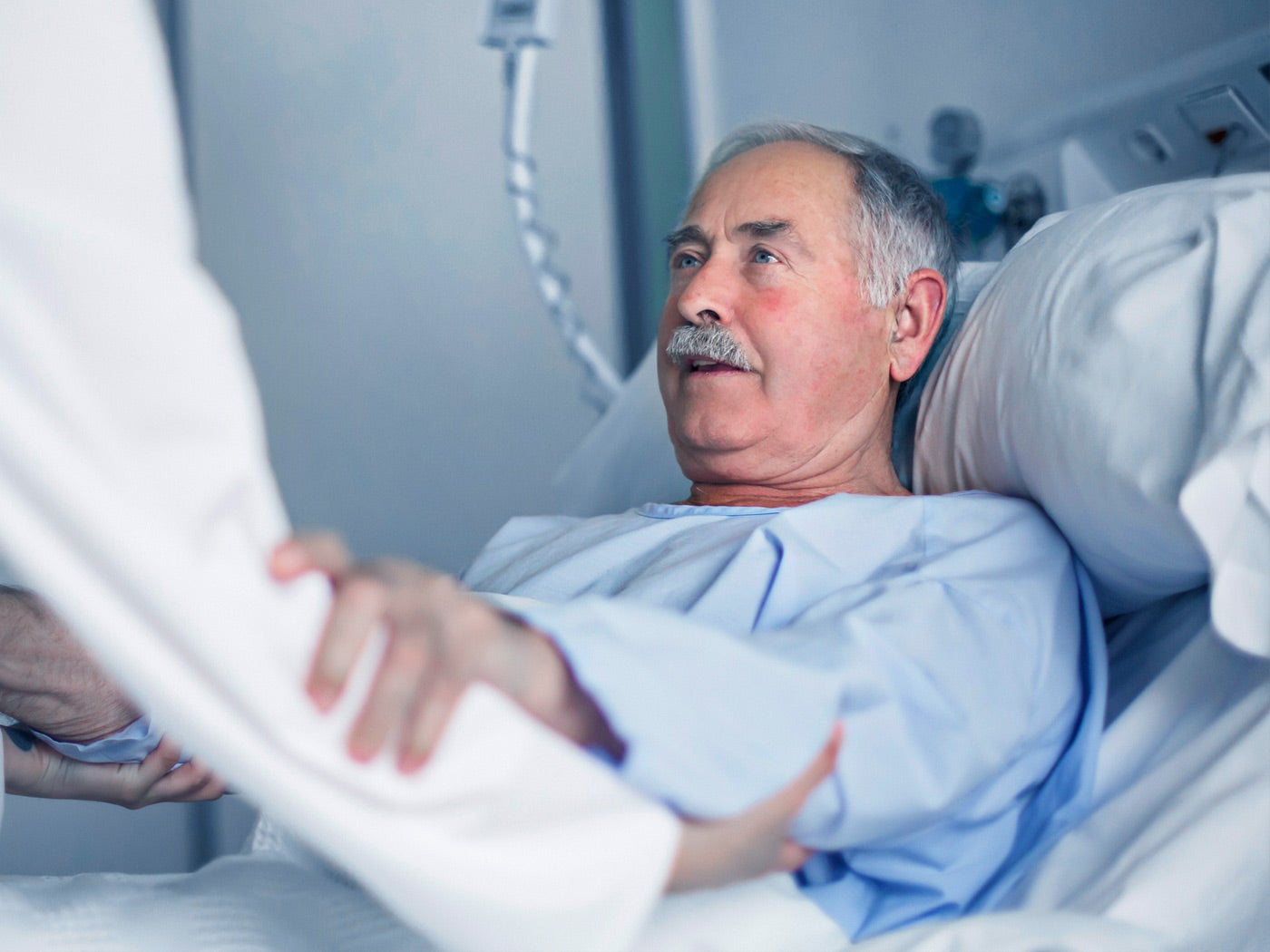Preventing Pressure Injuries Male patient in hospital bed, holding nurse’s arm.