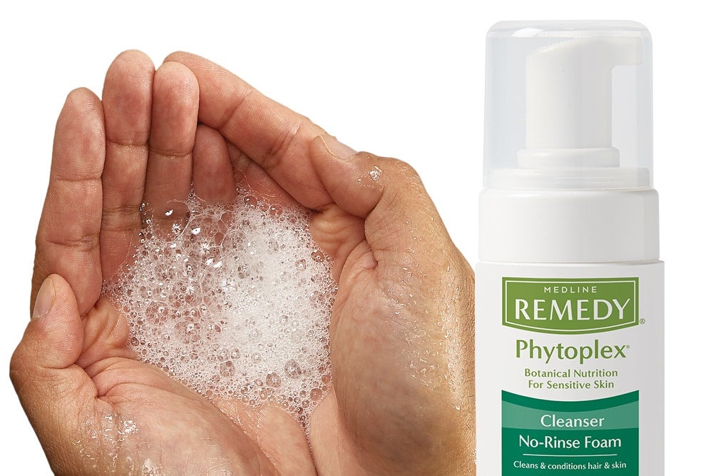 Hands cupped with foam cleanser next to container of Medline Phytoplex.