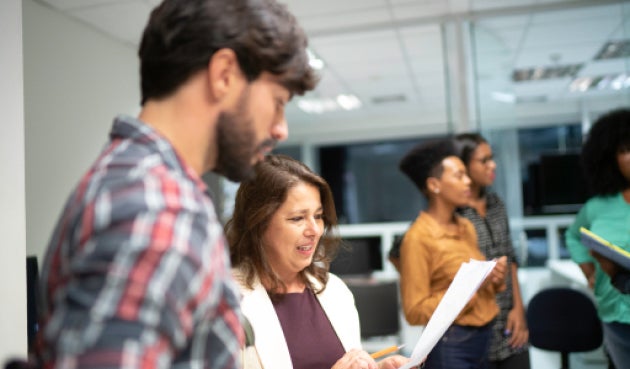 Group of people standing, including a woman looking at piece of paper. Group of people standing, including a woman looking at piece of paper.