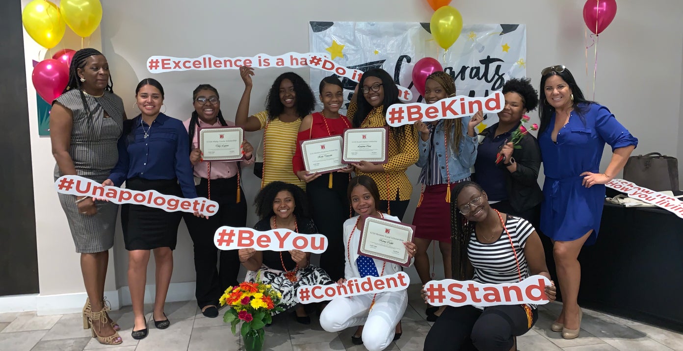 A portrait of a dozen women holding up signs and certificates. A portrait of a dozen women holding up signs and certificates.