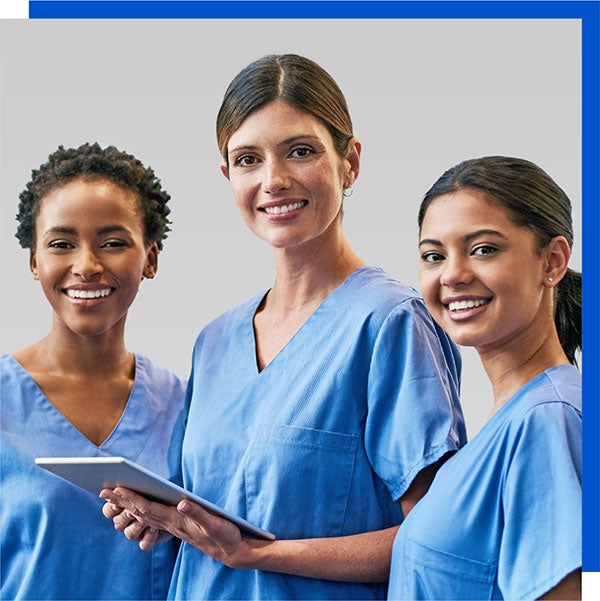 care-team Photo of three smiling women wearing blue short sleeved scrubs. Person in middle is holding a tablet.
