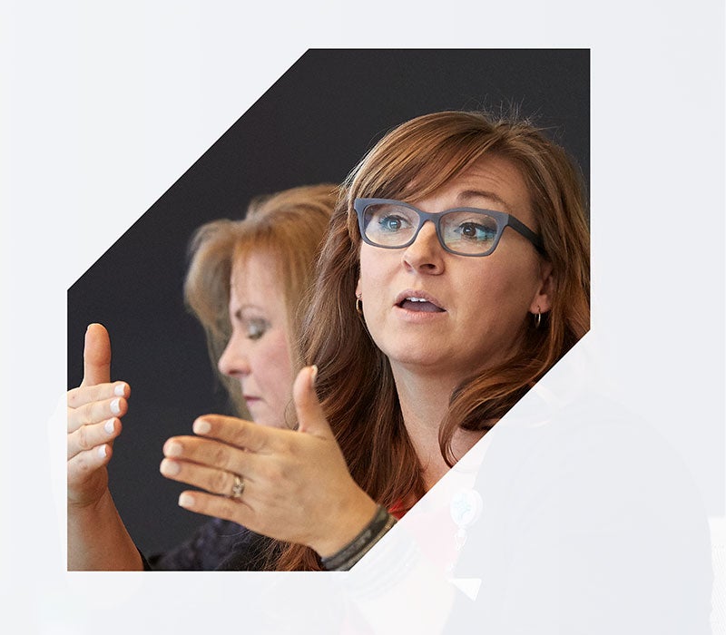 leadership Picture of two women one wearing glasses speaking with hands raised in emphasis. Photo partially covered by a graphic