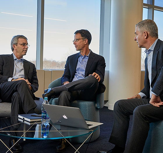 brand-book-final Three men in suits discussing around a laptop