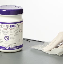 EVS worker's gloved hand disinfecting a table using a germicidal wipe