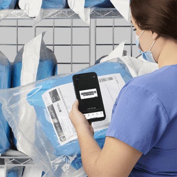 Real_time_info A tech in blue scrubs and a mask using an iphone to scan a barcode on a surgical pack.