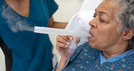 African-American woman with blowing into a nebulizer as clinician looks on