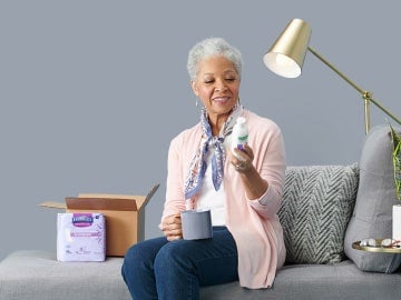 African-American woman, sitting on grey couch, reading the label on a bottle of body moisturizer Illustration of blue and grey boxes going into one large blue box representing product standardization
