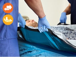 Reposition-gently Two clinicians holding handles of ComforGlide sheet under patient in bed; insets of orange friction icon and yellow shear icon
