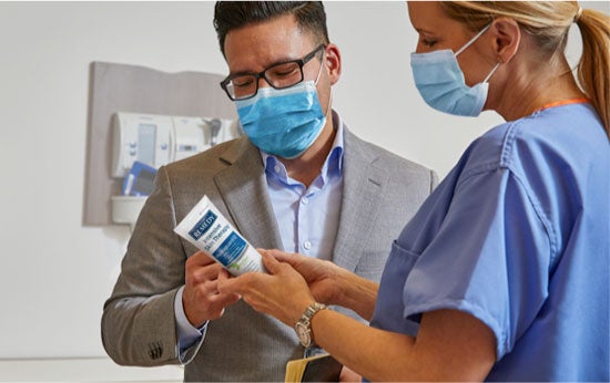 Masked Skin Health specialist shows a masked caregiver a skin care product